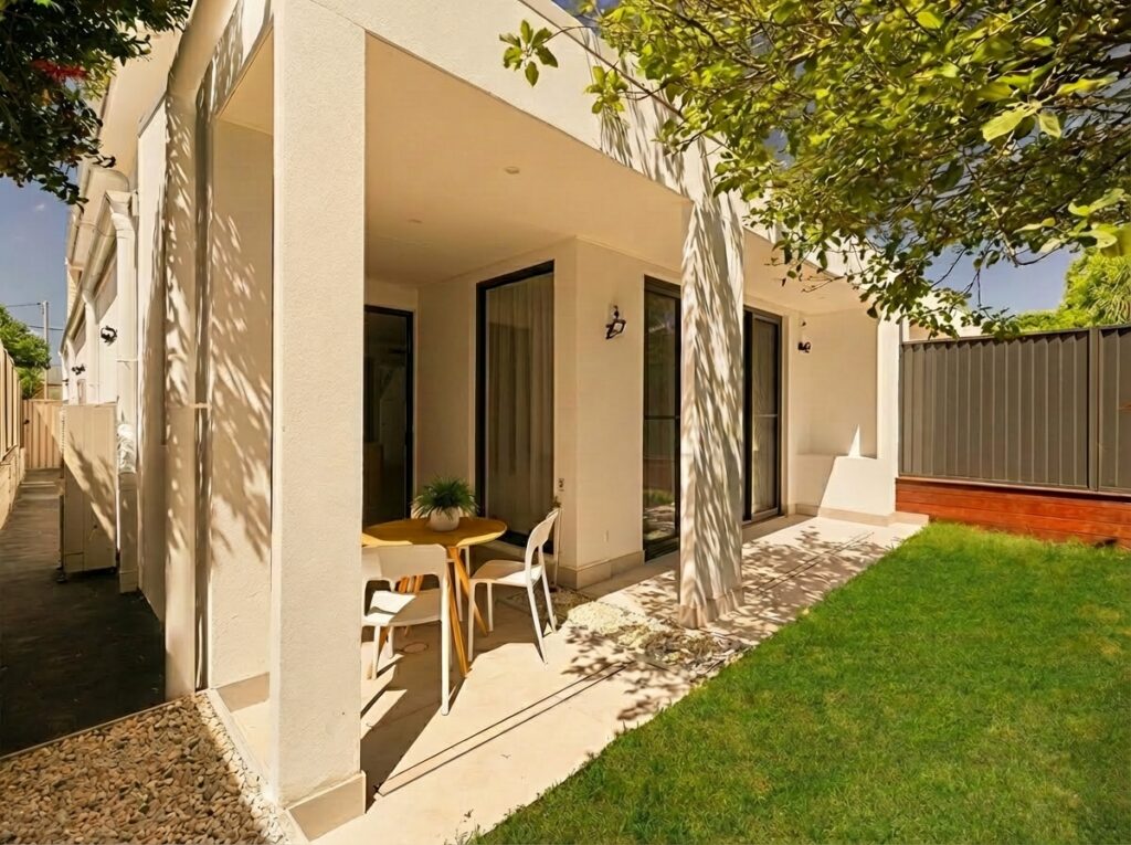 A private outdoor alfresco and backyard area at 8 Kinross Place, Revesby, featuring a clean white stucco finish and minimalist patio furniture by Zand Design.